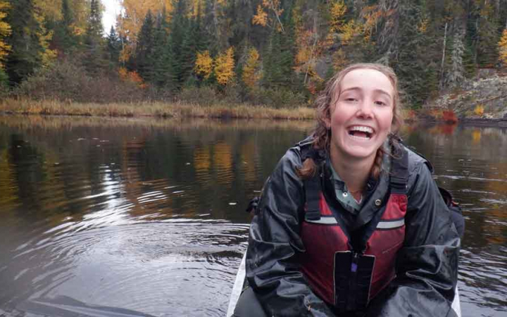 a young person wearing life jacket sits in a canoe and smiles at the camera